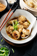 Sesame Chicken Dumplings in Spicy Broth with Garlic Crisps. Black background.