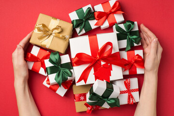 First person top view photo of female hands hugging stack of gift boxes with ribbon bows on isolated red background