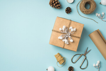 Top view photo of giftbox decorated with snow twig and twine white christmas tree balls and pine cones on isolated pastel blue background with blank space