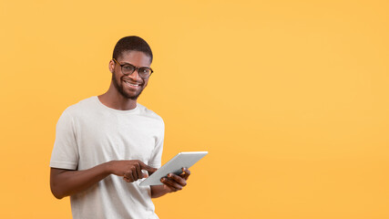 Portrait of happy black man using digital tablet and smiling to camera, standing over yellow background, copy space