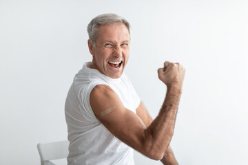 Joyful Vaccinated Senior Male Showing Biceps Over Gray Studio Background
