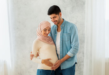 Parenthood concept. Loving arab pregnant woman and her husband embracing, smiling and touching belly