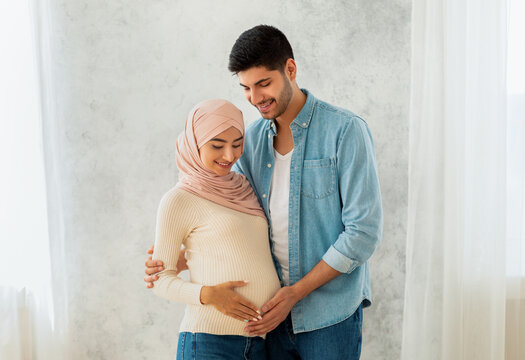 Parenthood concept. Loving arab pregnant woman and her husband embracing, smiling and touching belly