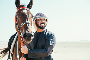Young adult with Kandura, the emirates traditional clothes, riding his horse in the desert
