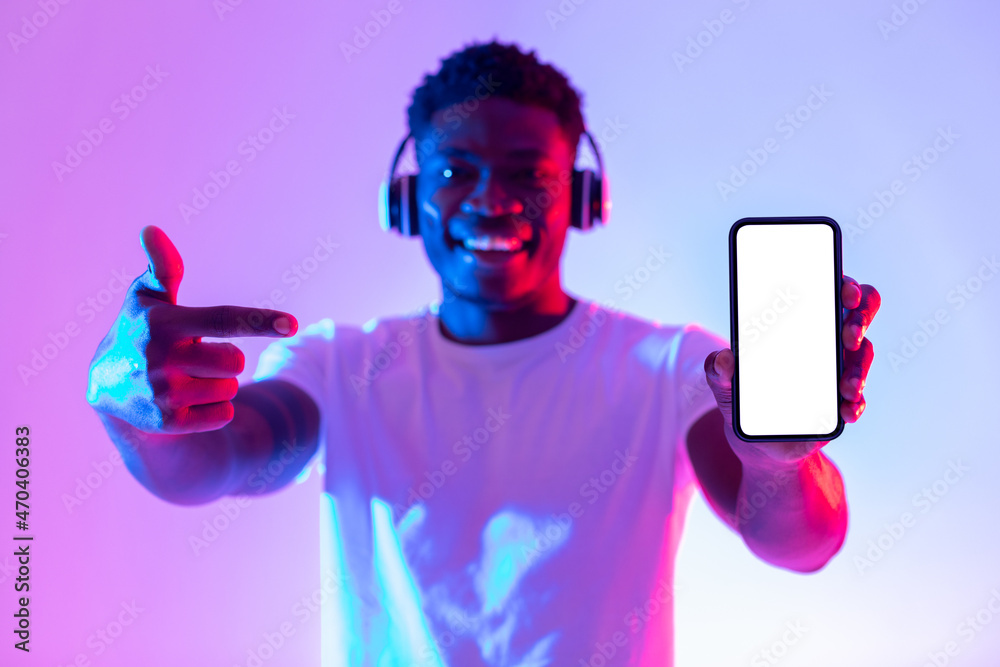 Poster check out new music app. happy black guy in headphones pointing at smartphone with empty screen in n