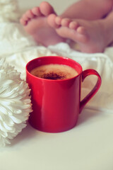 A cup of coffee or hot chocolate and white chrysanthemum and female bare feet