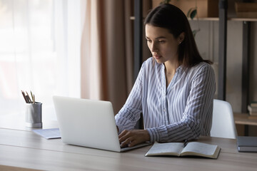 Focused smart beautiful young businesswoman typing message on email response on computer,...