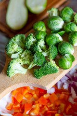 Brussels sprouts, broccoli, chopped red sweet pepper, onion and zucchini on a wooden cutting board.