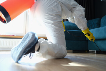 A man in a protective suit sprays under the couch - obrazy, fototapety, plakaty