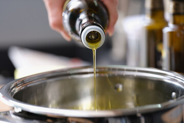 Olive oil is poured from a bottle into a saucepan
