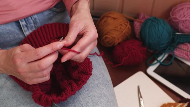 A woman knits a hat from woolen yarn. Self made. Colored yarns and knitting needles.