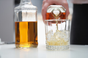 A man pours a strong alcoholic drink into a glass with ice