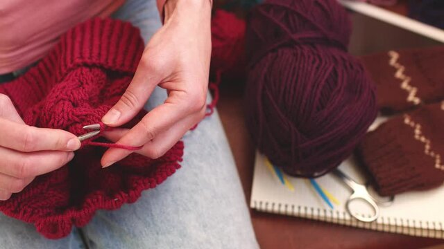 A woman knits a hat from woolen yarn. Self made. Colored yarns and knitting needles.