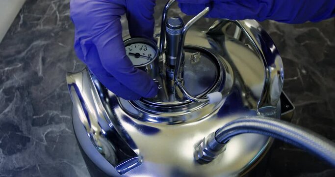 A man in blue gloves installs a cap with a pressure gauge on a sterile chrome-plated tank of liquid. Preparing the high pressure tank for liquid filtration.