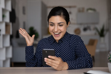 Overjoyed sincere young Indian ethnicity woman looking at cellphone screen, getting message with amazing unbelievable good news, celebrating online lottery betting gambling auction win or job offer.