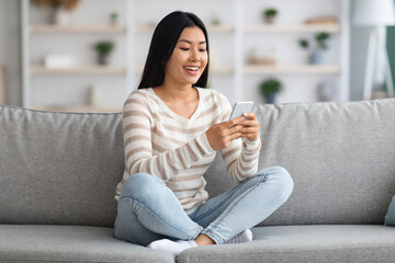Obraz premium Young Asian Woman Using Smartphone While Resting On Sofa At Home