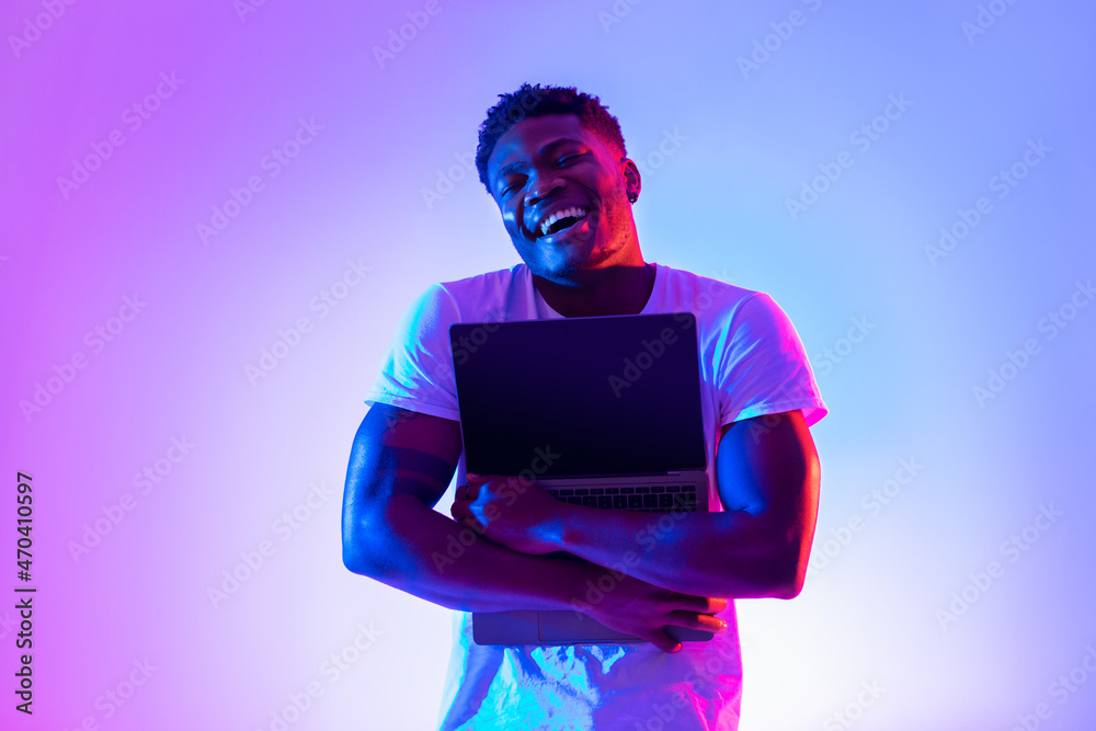Poster technology lover concept. happy black man hugging laptop with blank screen in neon light, mockup for