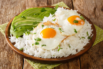 Boiled rice on top with fried eggs served with fresh avocado close-up in a plate on the table. horizontal