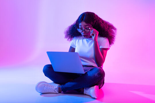 Deadline concept. Full length of surprised black woman using laptop computer, opening mouth in shock in neon light