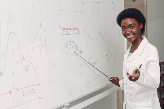 African American Smiling Black Woman Math Teacher Stands At White Board With Pointer.