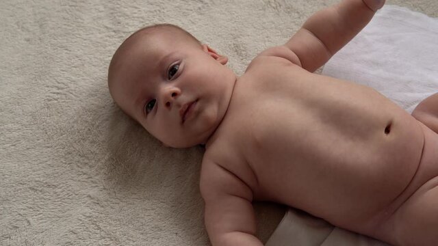 Childhood, motherhood, family, hygiene, infant concept Close-up Happy playful nake kid 2 month newborn boy looking at camera after bath shower on white soft bed. baby child waking time before bedtime
