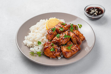 A portion with chicken teriyaki with rice and sauce on a gray background.