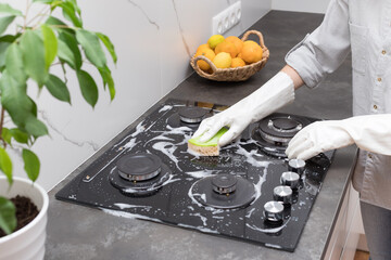 Woman in rubber gloves cleaning gas stove top with sponge and detergent. Clean house and hygiene...