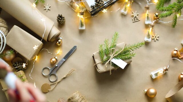 Hands pack a gift for Christmas and new year in eco-friendly materials: kraft paper, live fir branches, cones, twine, tied with a bow. Tags with mock up, natural decor, hand made, flatly. Festive mood