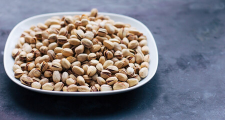 A white plate with rav pistachios in a shell shell on a dark gray background