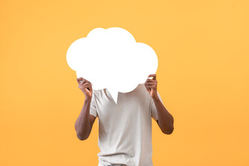 Faceless african american man covering his face with white speech bubble, standing over yellow...
