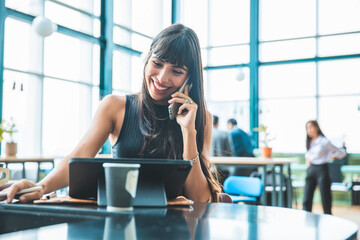 Cafe city lifestyle woman drinking coffee texting text message on smartphone or tablet  sitting indoor in trendy urban cafe. business woman working with laptop on a wood table.