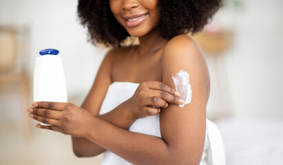 Unrecognizable young black woman applying lotion on her body, pampering skin afterbath or shower at...
