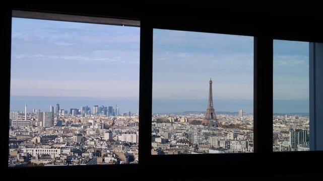 Vue panoramique sur la ville de Paris, avec la tour Eiffel et le quartier de La D&eacute;fense, depuis la fen&ecirc;tre / baie vitr&eacute;e d&rsquo;un appartement parisien en &eacute;tage &eacute;lev&eacute; (France)