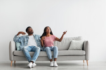 Young black woman switching on air conditioning at home
