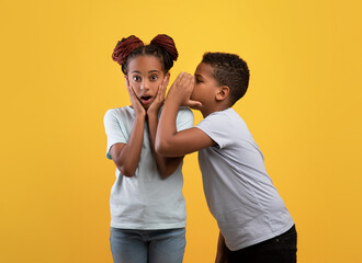 Black boy brother sharing secrets with his shocked sister