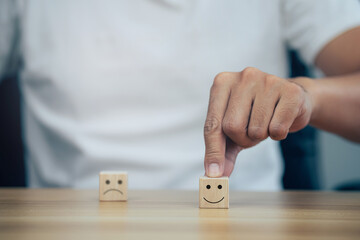 Satisfaction concept, Closeup man choose smiley face and blurred sad face icon on wood cube.