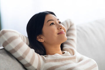 Portrait Of Calm Beautiful Young Asian Female Leaning Back On Comfortable Couch