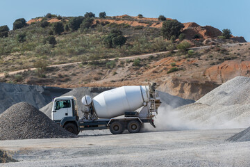 Concrete mixer truck driving between mountains of sand and gravel in a quarry.
