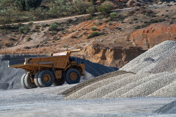 Huge dump truck driving past mountains of gravel in a quarry.