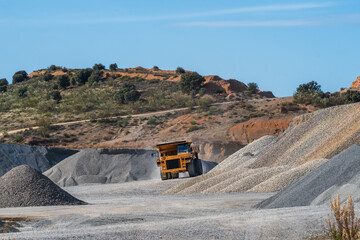 Huge dump truck driving past mountains of gravel in a quarry.