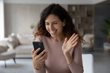 Head shot close up excited young woman waving hand at smartphone webcam, chatting online by video...
