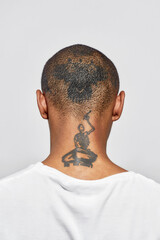 Back view of shaved tattooed head and neck of young dark skinned man posing isolated over white...
