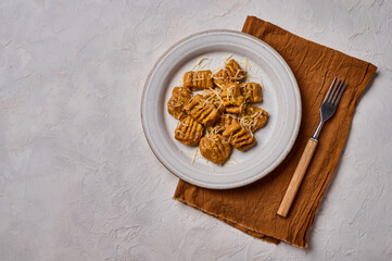 Mediterranean and Alpine vegetarian gnocchi from whole grain flour, baked pumpkin puree and parmesan on light plate with fork and napkin on concrete background. Top view