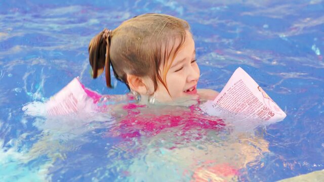 a funny little girl swims and plays in inflatable armbands in a pool