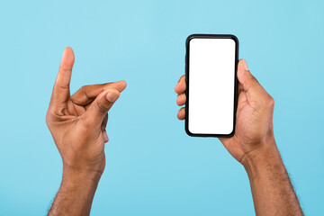 Cropped view of young black guy showing smartphone with empty white screen and holding something, mockup