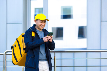 Happy male courier walking food supplier, looking forward to new order received in phone app, asian courier