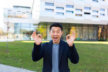Fototapeta premium Happy asian businessman looking at camera and smiling, male freelancer outside office