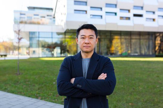 portrait handsome Asian man a university college teacher, businessman, scientist or educator. Standing background modern office center or campus with arms crossed Outside, outdoors looking at camera