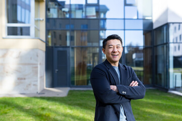 portrait handsome Asian man a university college teacher, businessman, scientist or educator. Standing background modern office center or campus with arms crossed Outside, outdoors looking at camera - obrazy, fototapety, plakaty