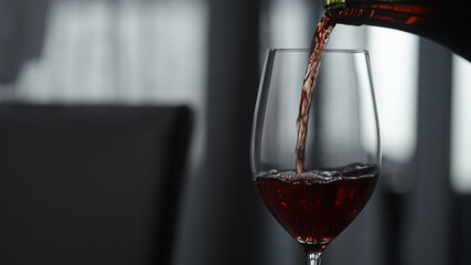 pour red wine in wineglass indoor with window on background